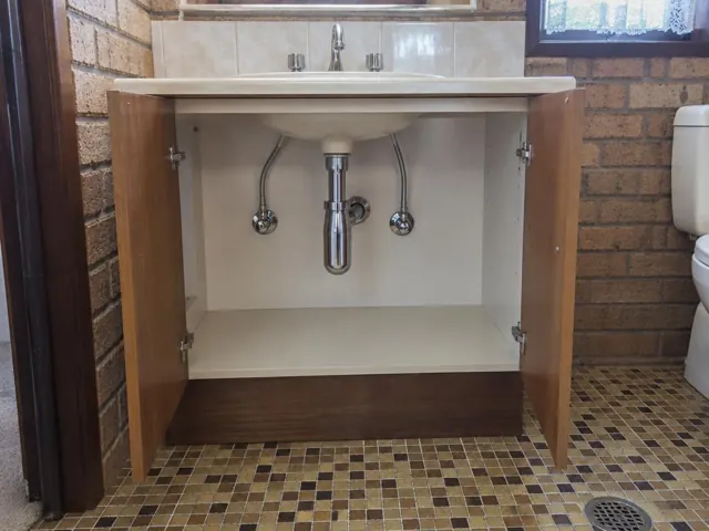 Open vanity under a sink with neat pipe access and dry wall inside a brick-lined bathroom in Greystanes
