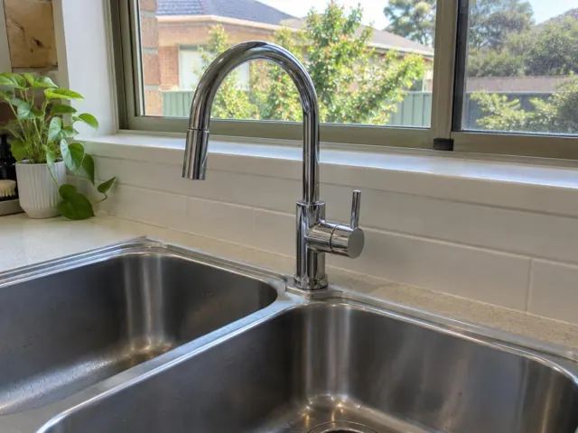 Chrome kitchen sink tap above a double stainless steel sink with white tiled splashback in Lidcombe